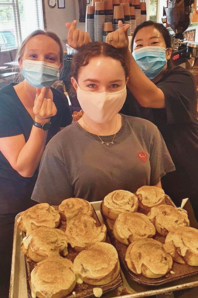 Cheerful Black Cottage Cafe staff presenting freshly baked cinnamon rolls, highlighting our homemade treats.